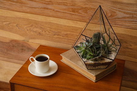 Florarium with book and cup of coffee on table near wooden wallの写真素材