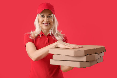 Mature courier with pizza on red backgroundの写真素材