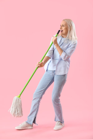 Mature woman with mop singing on pink backgroundの写真素材