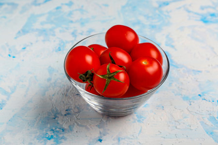 Glass bowl with fresh cherry tomatoes on blue backgroundの写真素材