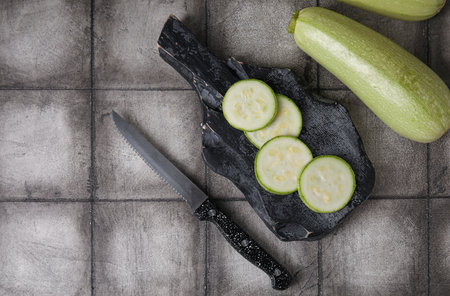Wooden board with cut and whole zucchini on black tile backgroundの写真素材