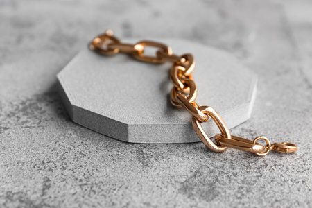 Decorative podium with beautiful golden chain bracelet on grunge gray backgroundの写真素材