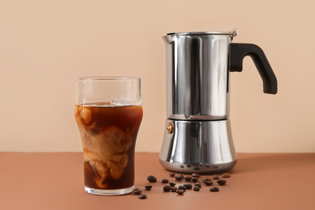 Glass of ice coffee with beans and geyser coffee maker on table near beige wallの写真素材