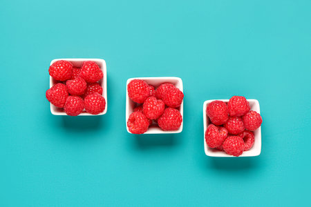 Bowls with fresh raspberries on blue background