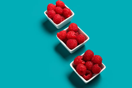 Bowls with fresh raspberries on blue background
