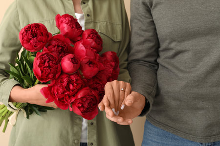 Happy engaged couple with flowers holding hands on beige background, closeupの写真素材