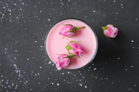 Glass of panna cotta with beautiful pink rose flowers on black tableの写真素材