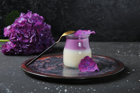Glass of panna cotta with beautiful hydrangea flowers on black tableの写真素材