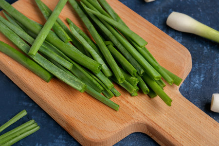 Board with fresh green onion on blue background