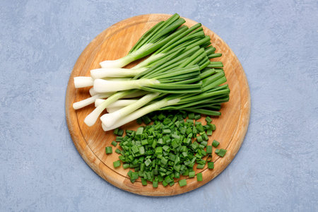 Board with slices of fresh green onion on blue background