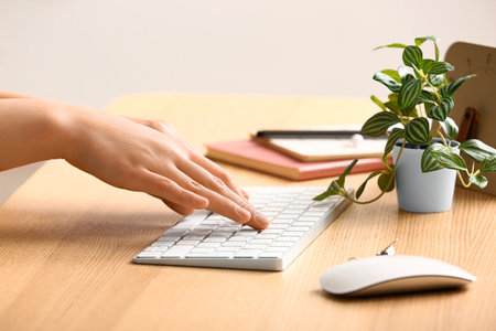 Female programmer using computer keyboard with mouse and houseplant on wooden table, closeupの写真素材