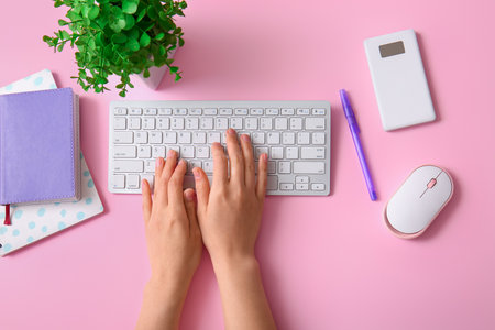 Female programmer using computer keyboard with mouse and notebooks on pink backgroundの写真素材