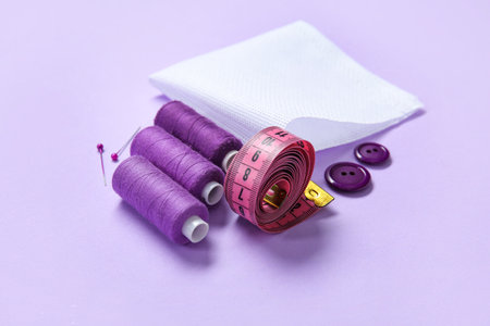 Canvas with buttons, thread spools and measuring tape on lilac backgroundの写真素材