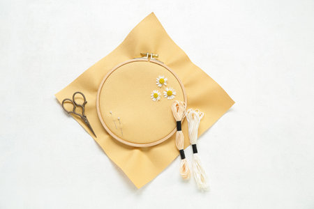 Wooden embroidery hoop with scissors, mouline threads and chamomile flowers on white background