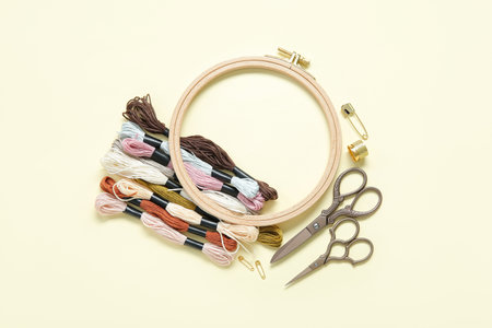 Wooden embroidery hoop with scissors, mouline threads and thimble on pale yellow backgroundの写真素材