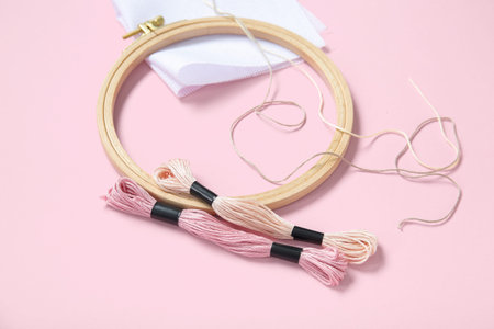 Wooden embroidery hoop with mouline threads, pins and canvas on pink background