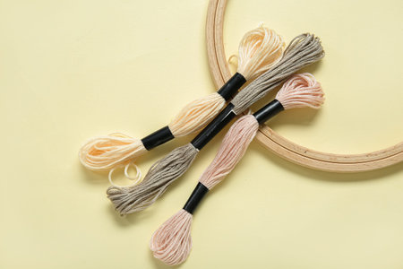 Wooden embroidery hoop with mouline threads on pale yellow background