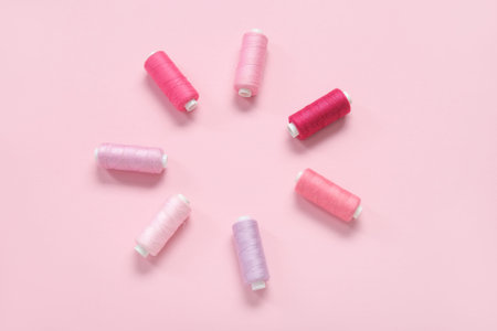 Frame made of different thread spools on pink background