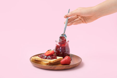 Woman holding spoon with strawberry jam and tasty toasts on pink backgroundの写真素材