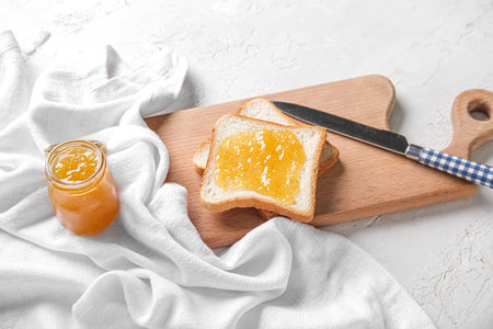 Wooden board with tasty toasts, jar of peach jam and knife on grunge white backgroundの写真素材
