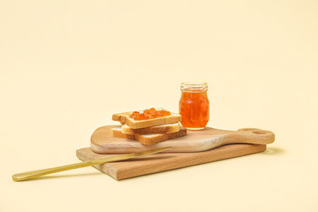 Wooden boards of tasty toasts, apricot jam and knife on pale yellow backgroundの写真素材