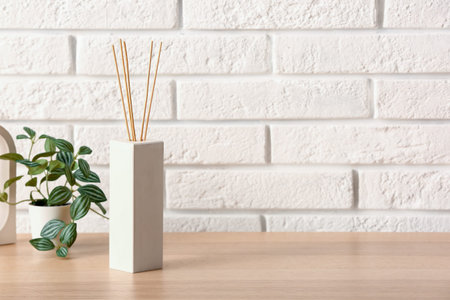 Bottle of reed diffuser and houseplant on table near light brick wall in room