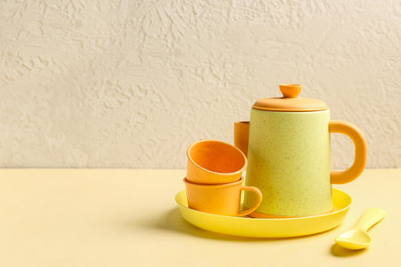 Plate with cups, teapot and spoon for baby on yellow tableの写真素材