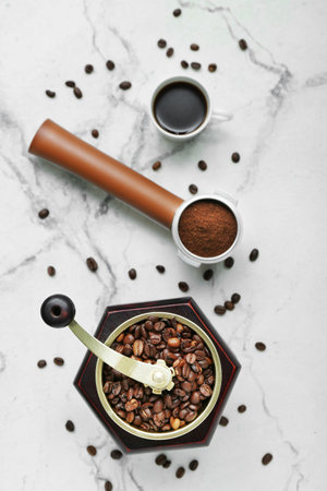 Cup of hot espresso, coffee grinder, beans and portafilter on white marble backgroundの写真素材