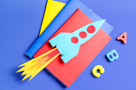 Paper rocket with notebooks and wooden letters on dark blue backgroundの写真素材
