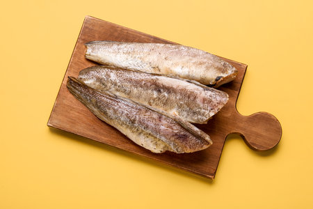 Wooden board with raw codfish on yellow backgroundの写真素材
