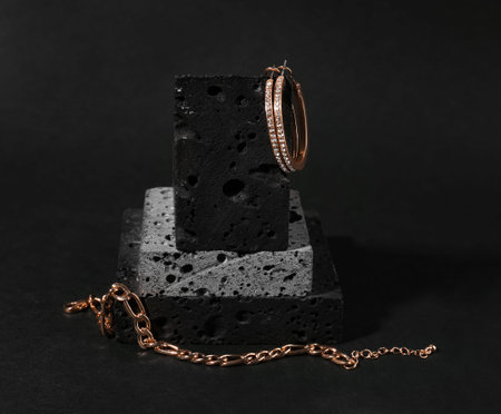 Decorative podium with beautiful chain bracelet and earrings on black background