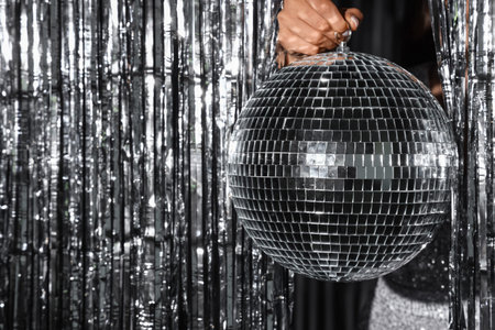 Woman holding disco ball against silver tinsel