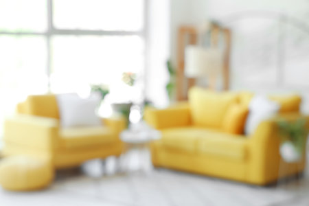 Interior of light living room with yellow sofa and armchair near big window, blurred viewの写真素材