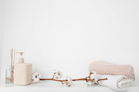 Cotton sprig with scented sticks, soap dispenser and towels on white shelf