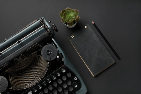 Vintage typewriter with notebook, pencil and succulent on black background