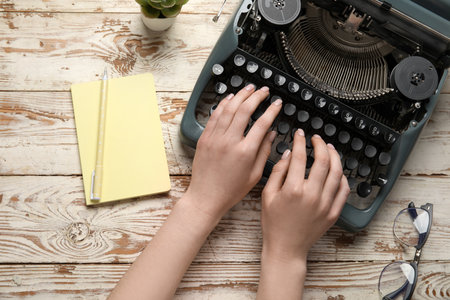Woman typing on typewriter with eyeglasses, notebook and houseplant on wooden backgroundの写真素材