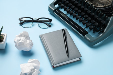 Vintage typewriter with crumpled paper, eyeglasses and notebook on blue backgroundの写真素材