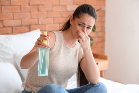Displeased young woman with air freshener in bedroom