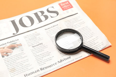 Mini magnifier and newspaper with headline JOBS on orange background. Search conceptの写真素材