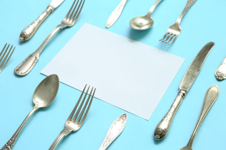 Frame made of blank card and stainless steel cutlery on blue background