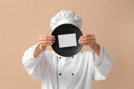 Female chef holding plate with blank card on beige backgroundの写真素材