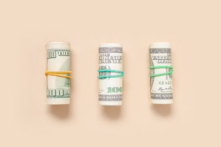 Rolls of one hundred dollar banknotes tied with rubber bands on beige backgroundの写真素材