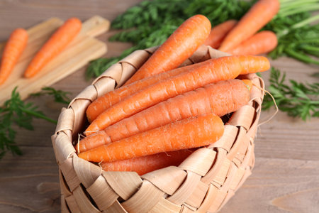 Wicker basket and board with fresh carrots on wooden tableの写真素材