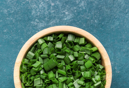 Bowl with slices of fresh green onion on blue background