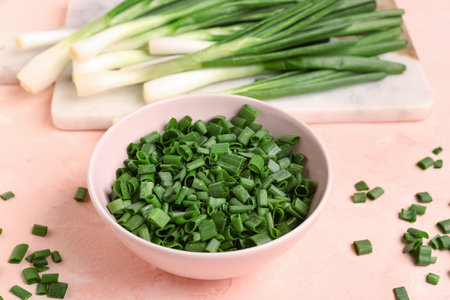 Bowl of slices and board with fresh green onion on pink backgroundの写真素材