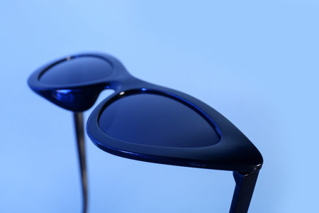 Stylish black sunglasses on blue background, closeup