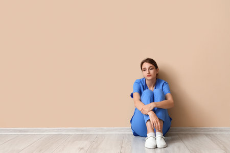 Sad female medical intern sitting near beige wallの写真素材