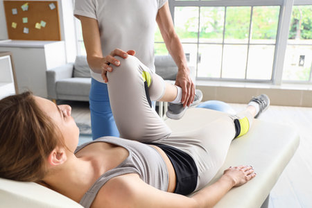 Female physiotherapist working with young woman on couch in rehabilitation center