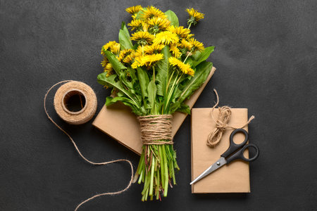 Bouquet of beautiful dandelion flowers, rope, scissors and books on dark backgroundの写真素材