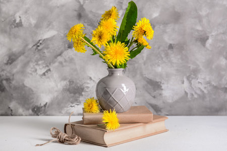 Vase with beautiful dandelion flowers, books and rope on light table against grunge backgroundの写真素材